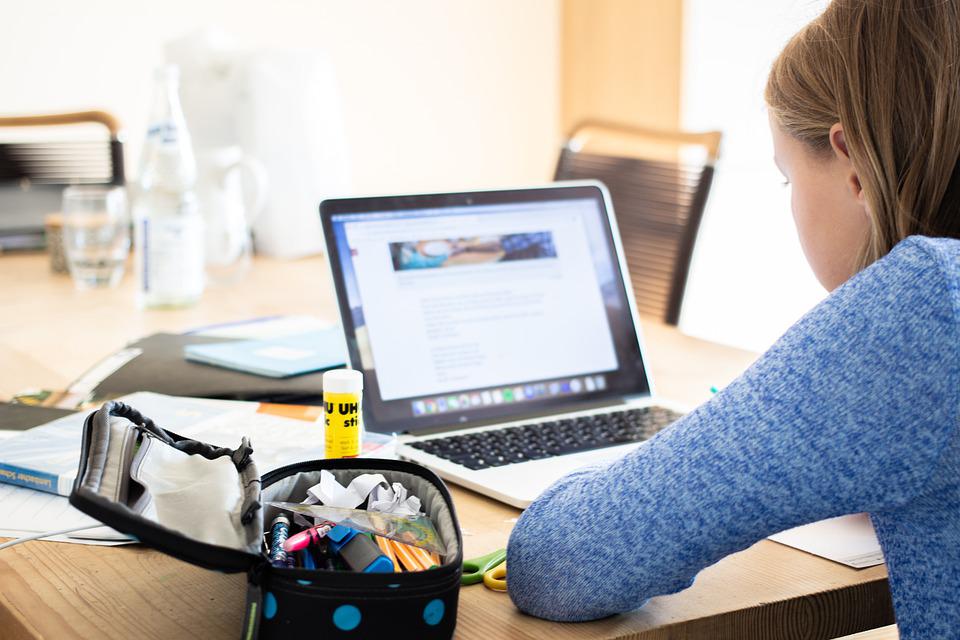 Niña leyendo texto en una laptop con cartuchera y útiles de escuela, todo apoyado sibre una mesa